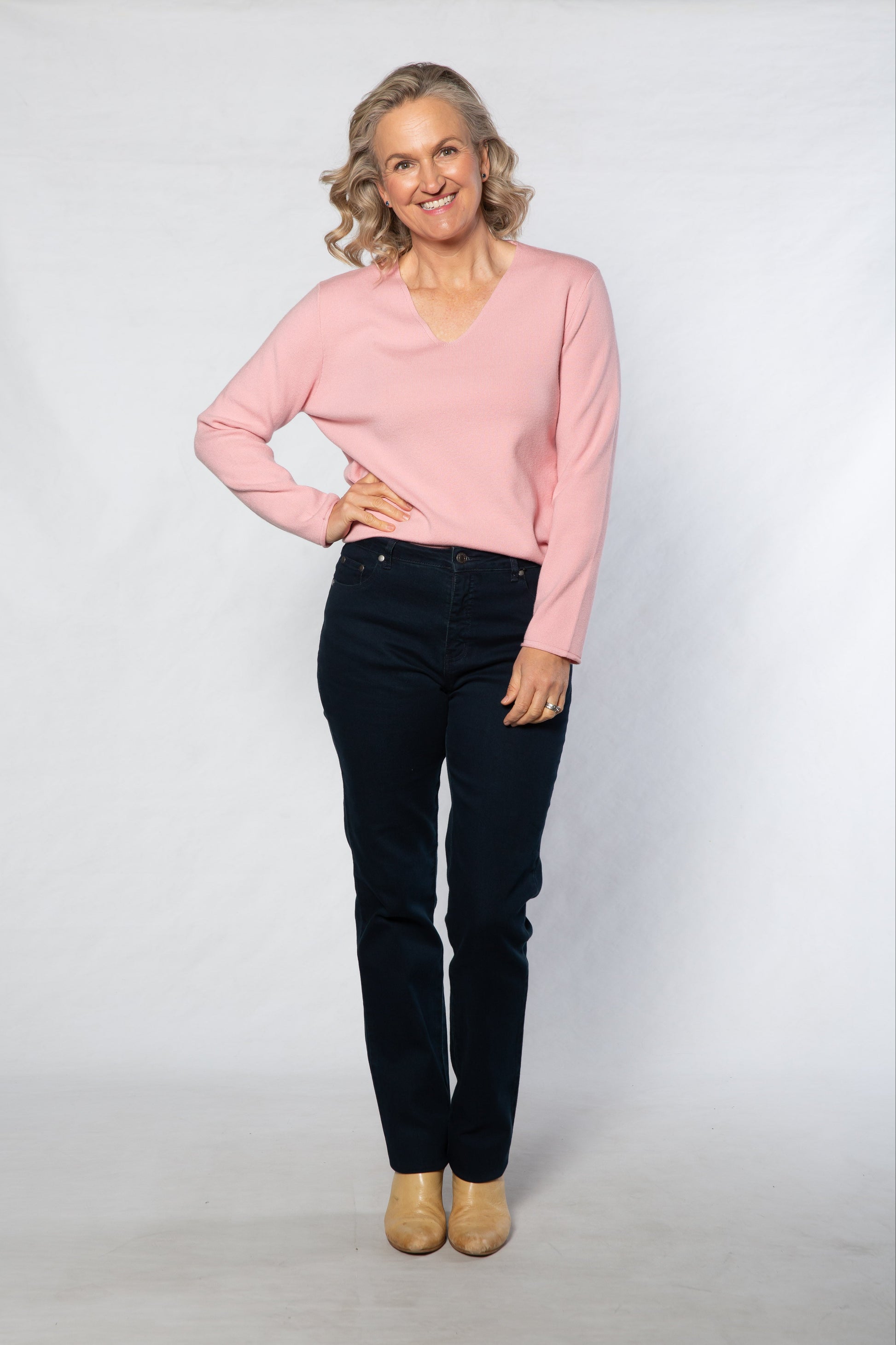 Woman wearing a pink sweater and black pants against a white background