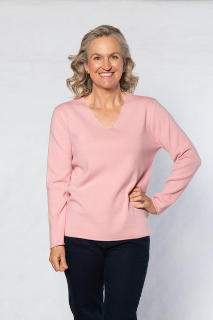 Woman wearing a pink sweater and black pants on a white background