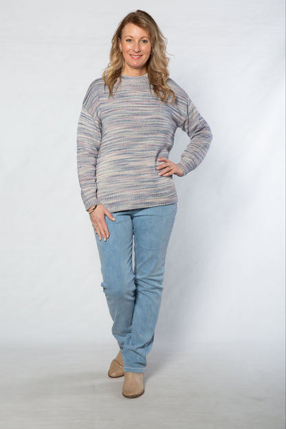 Woman wearing a striped sweater and blue jeans standing against a white background