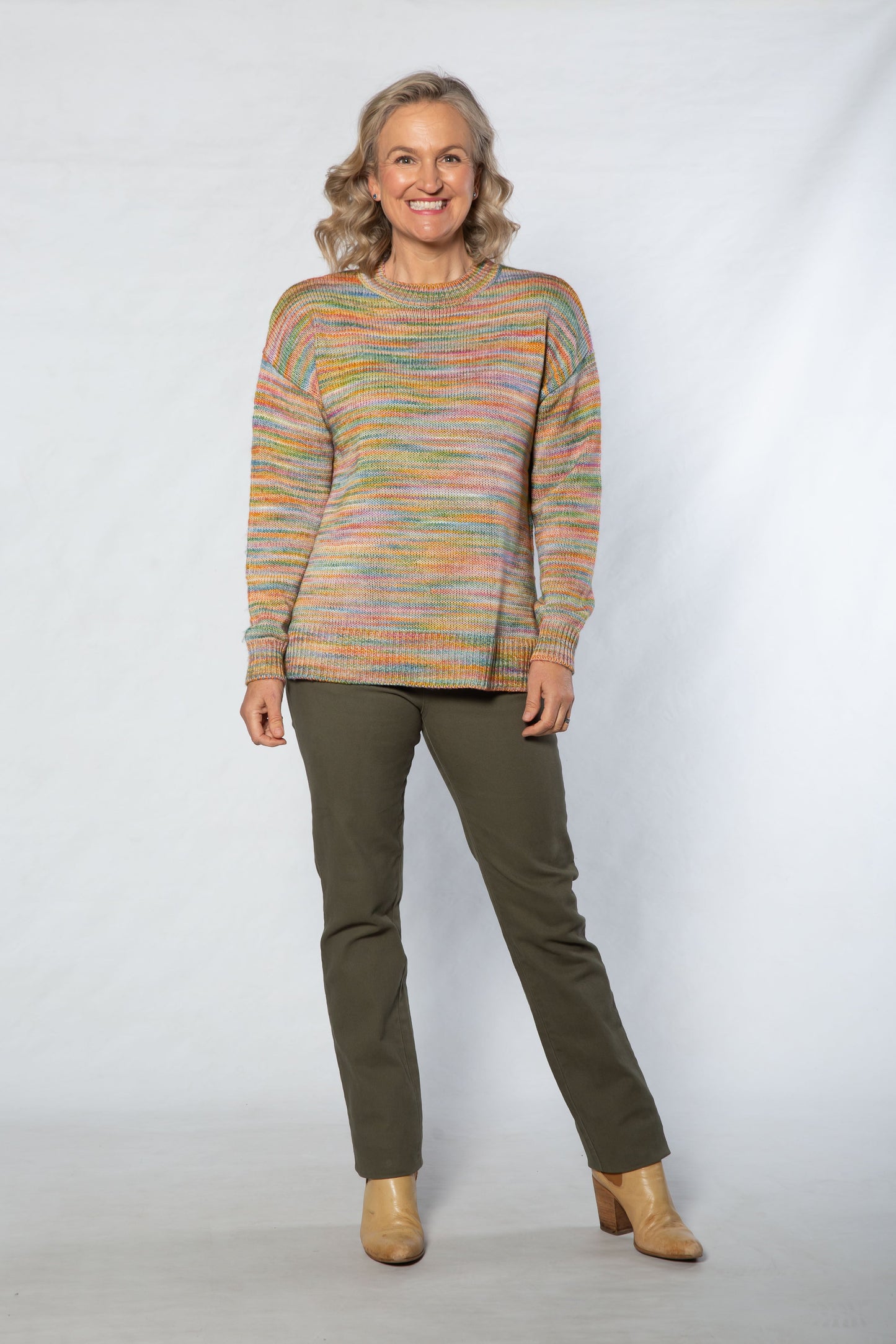 Woman wearing a colorful sweater and green pants against a white background