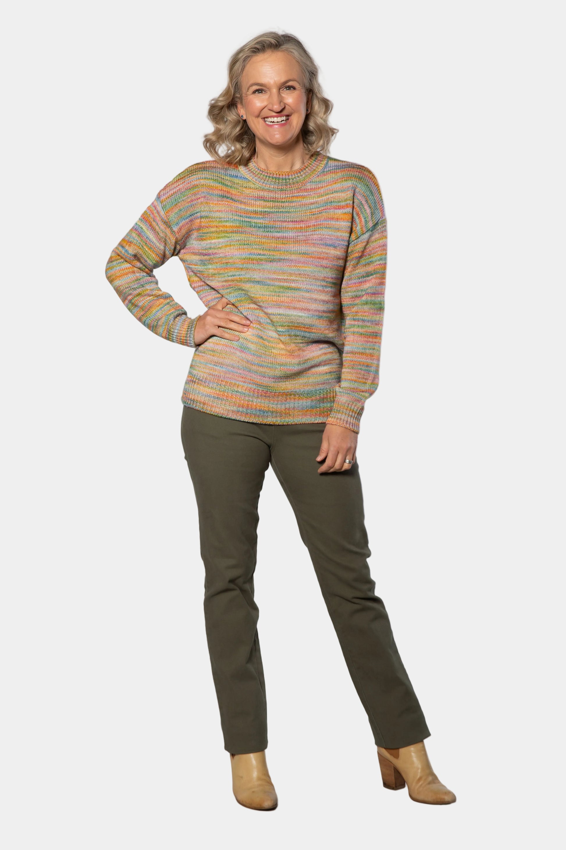 Woman wearing a colorful sweater and green pants against a white background