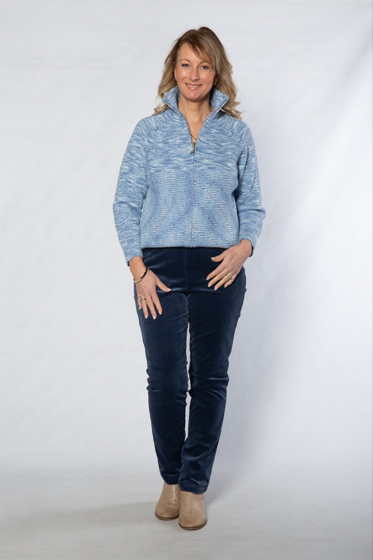 Woman wearing a blue sweater and dark jeans against a white background