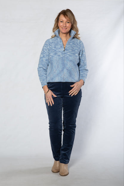 Woman wearing a blue sweater and dark jeans against a white background