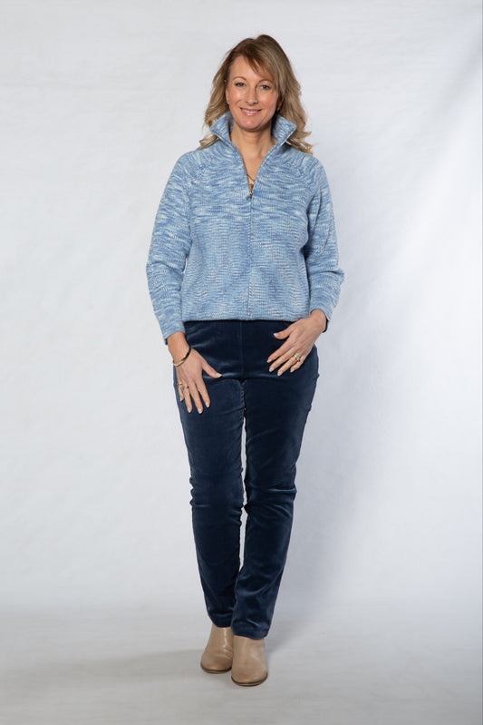 Woman wearing a blue sweater and dark jeans against a white background