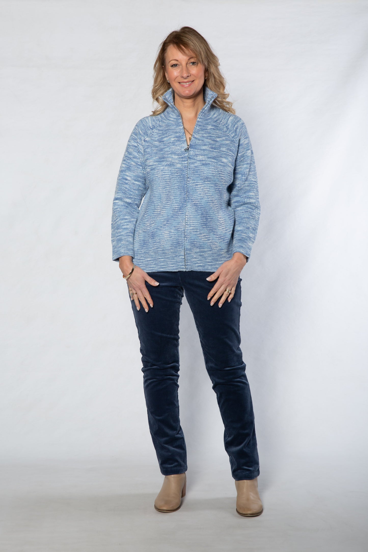 Woman wearing a blue patterned sweater and dark jeans against a white background