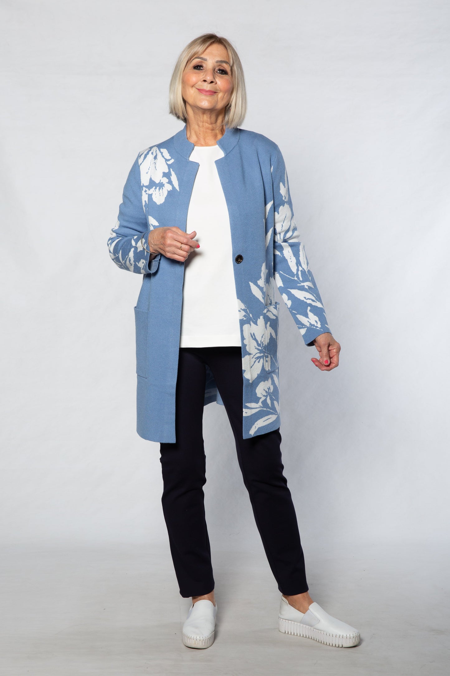 Person wearing a blue floral cardigan over a white shirt and black pants on a white background