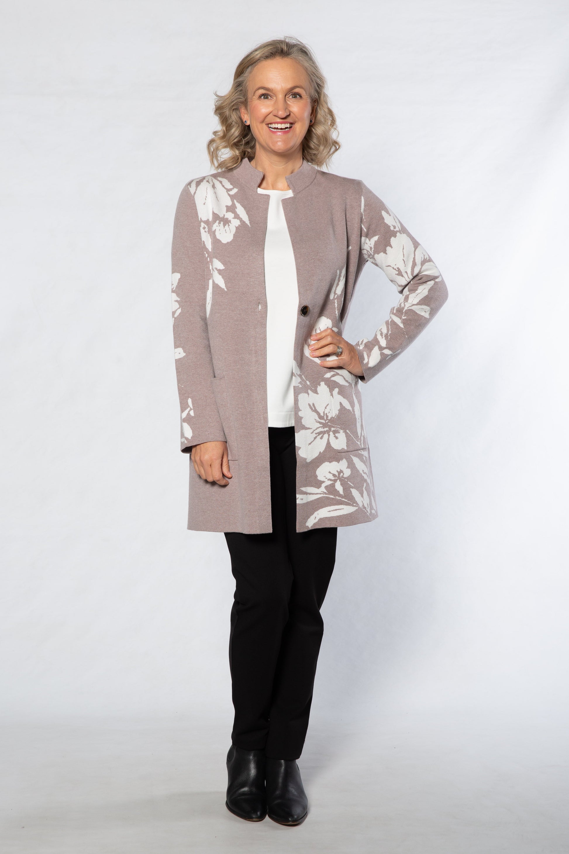 Woman wearing a patterned cardigan over a white shirt with black pants on a white background