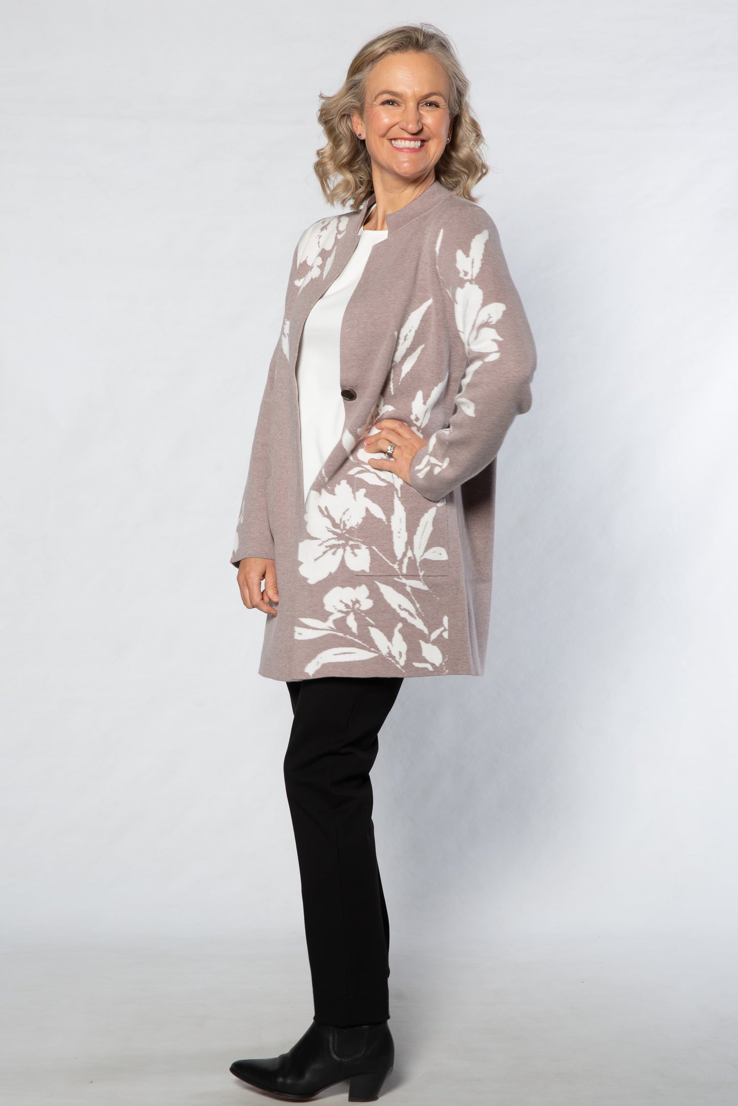 Woman wearing a floral cardigan over a white top with black pants on a white background