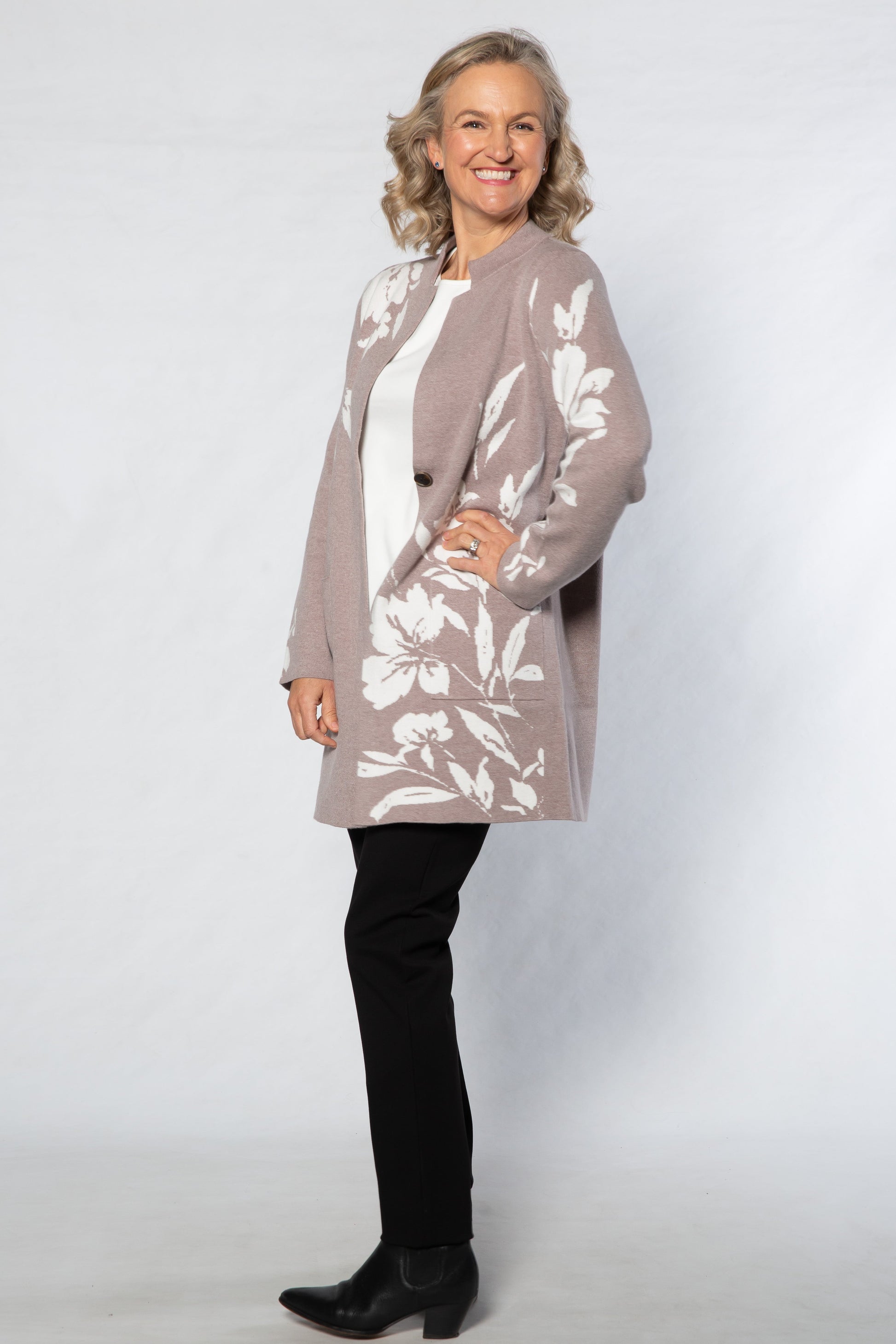 Woman wearing a floral cardigan over a white top with black pants on a white background
