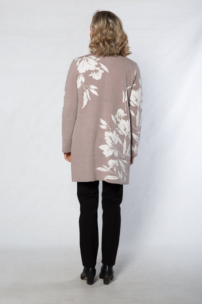 Person wearing a long, light brown cardigan with white floral patterns on a white background