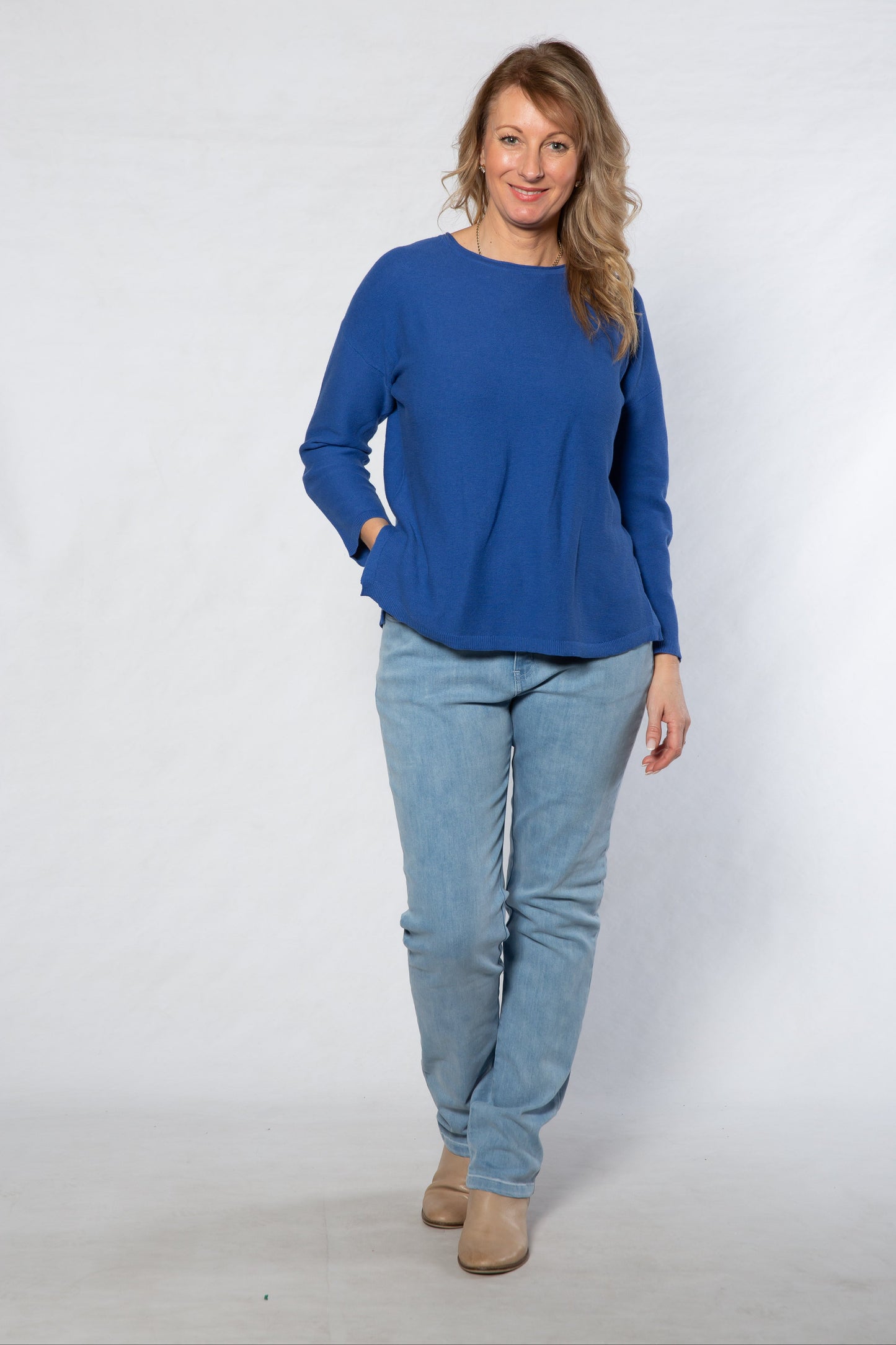 Woman wearing a blue top and light blue jeans against a white background
