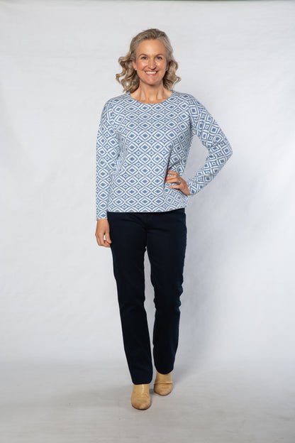 Woman wearing a blue patterned sweater and dark pants on a white background