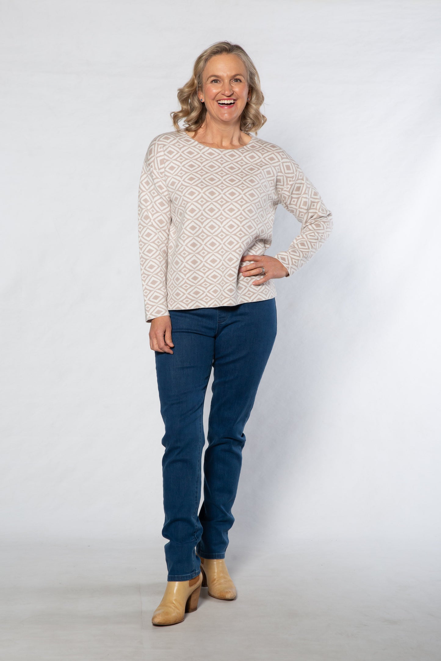 Woman wearing a patterned sweater and blue jeans against a white background
