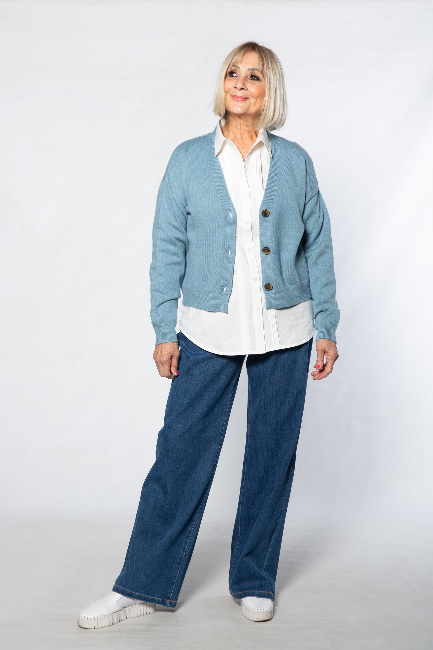 Person wearing a light blue cardigan, white shirt, and blue jeans on a white background