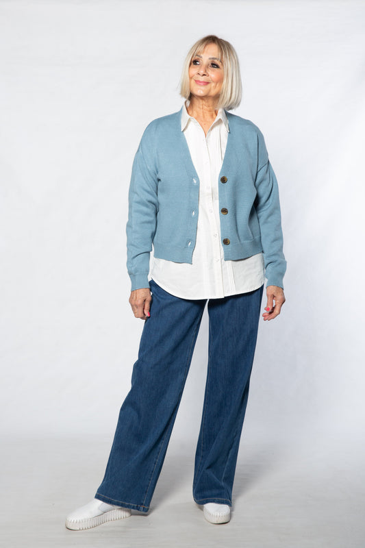 Person wearing a light blue cardigan, white shirt, and blue jeans on a white background