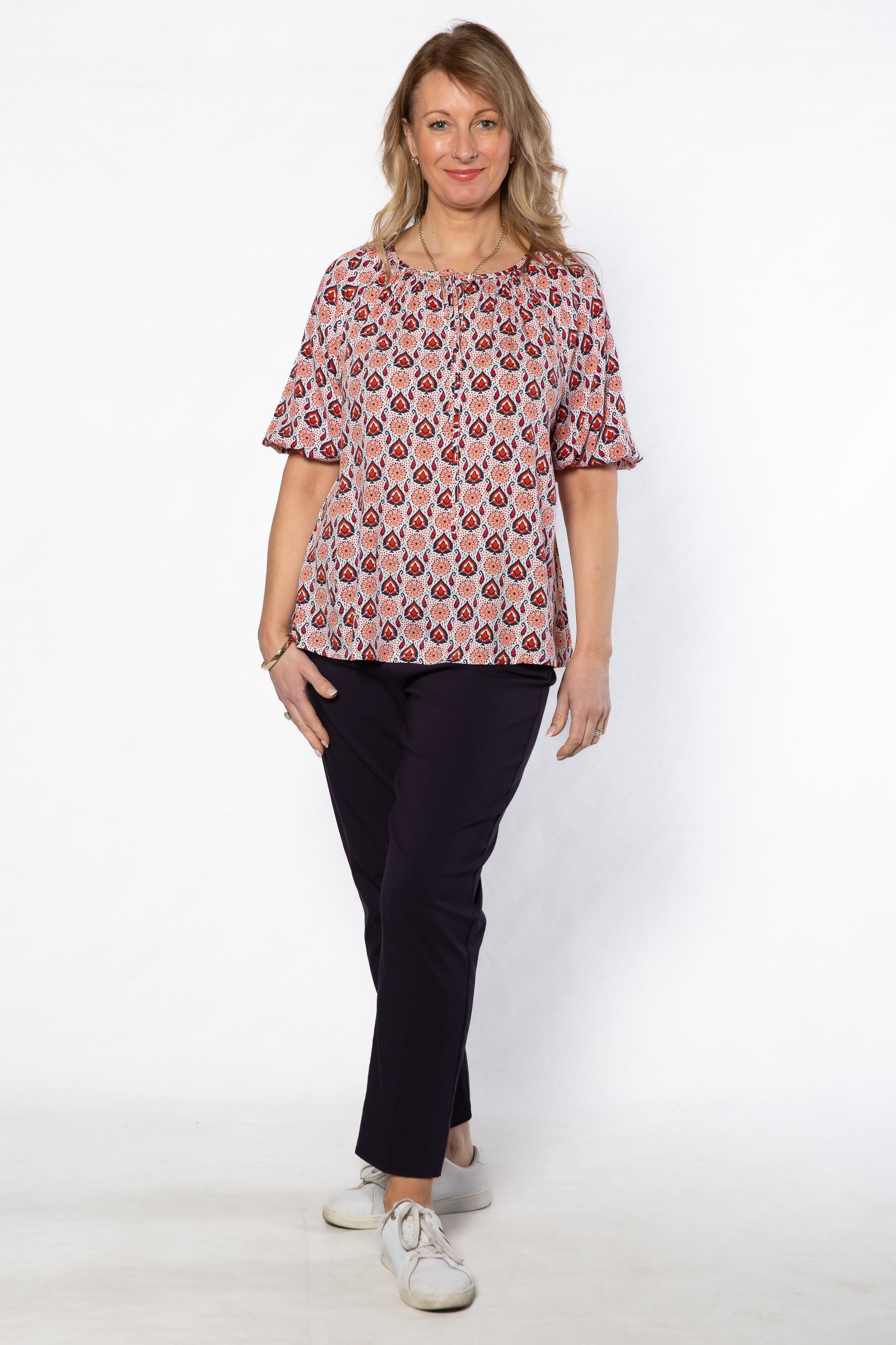 Woman wearing a patterned top and black pants on a white background