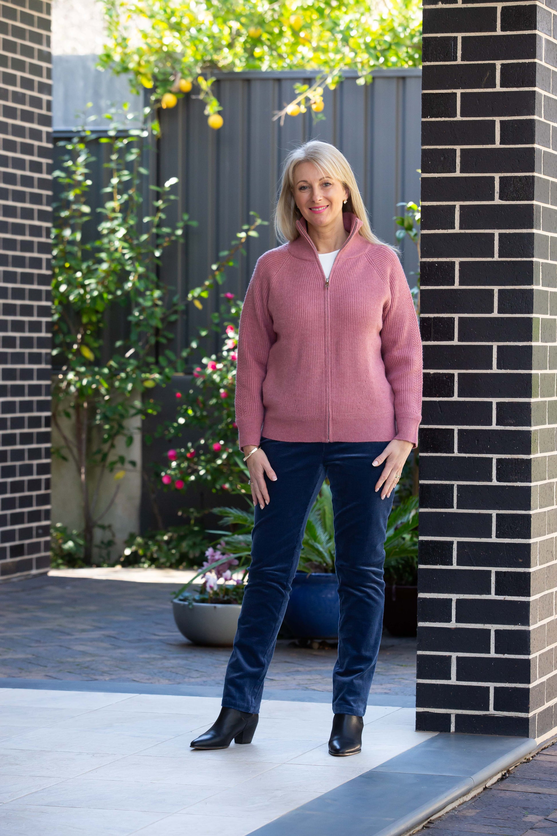 A model wearing storm blue corduroy pants with back patch pockets and a matching corduroy jacket, standing outdoors.