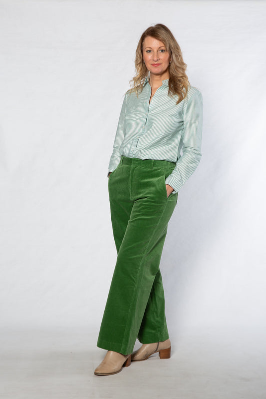 Woman wearing a light green shirt and green pants against a white background