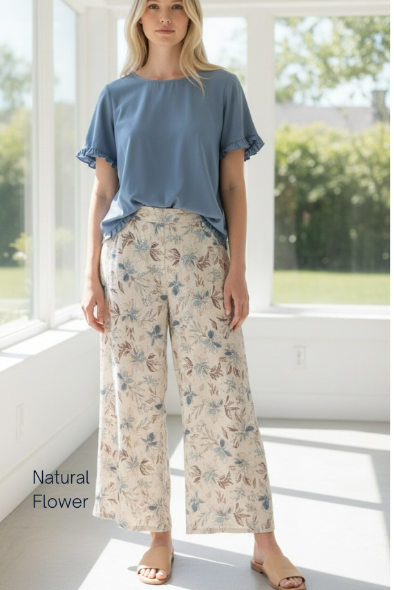 Woman wearing a blue top and floral pants in a bright room with large windows.