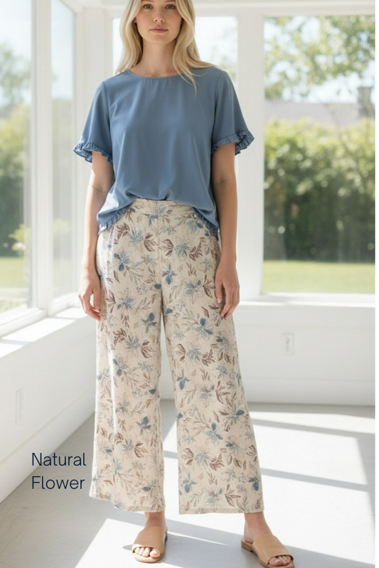 Woman wearing a blue top and floral pants in a bright room with large windows.