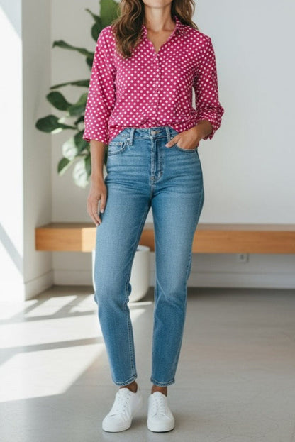 Person wearing a pink polka dot shirt, blue jeans, and white sneakers in a bright room.