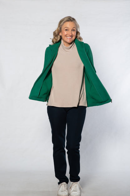 Person wearing a green coat, beige sweater, black pants, and white shoes on a white background