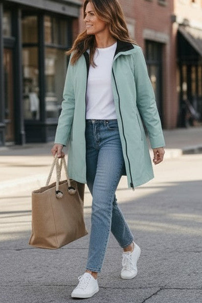 A woman walking outdoors on a city street wearing a light mint green coat over a white top and jeans, shown in two stacked views. The top view shows her from the waist up, and the bottom view shows her full body carrying a brown tote bag.