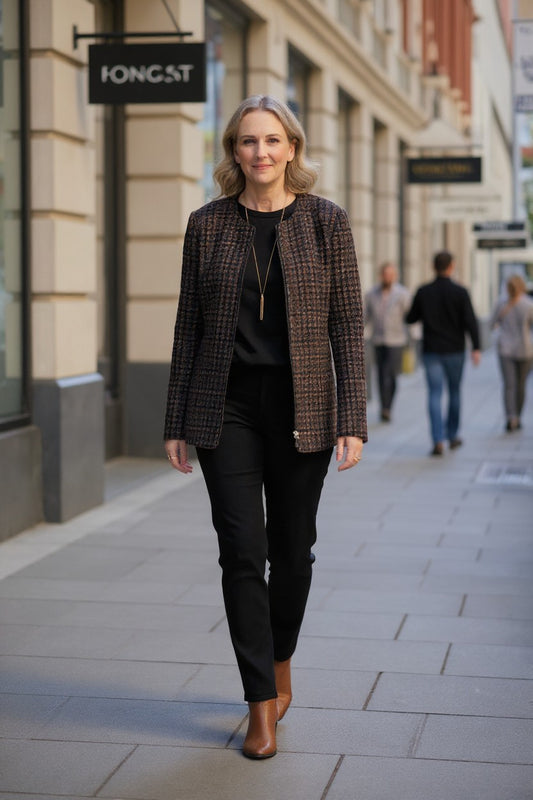 A woman walking down a city street wearing a brown and black houndstooth blazer, black top and trousers, and brown ankle boots.