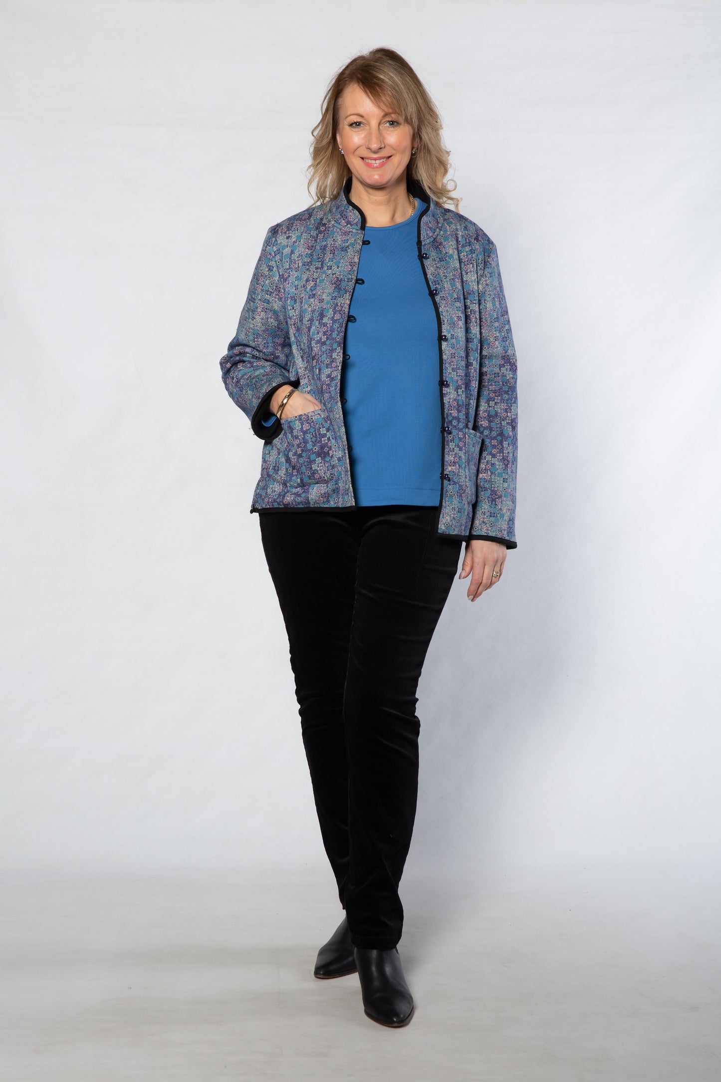 Woman wearing a patterned jacket over a blue shirt and black pants on a white background