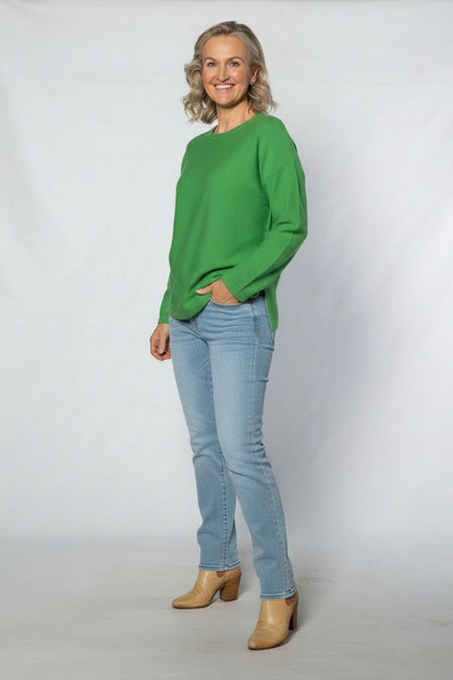 Woman wearing a green sweater and light blue jeans against a white background