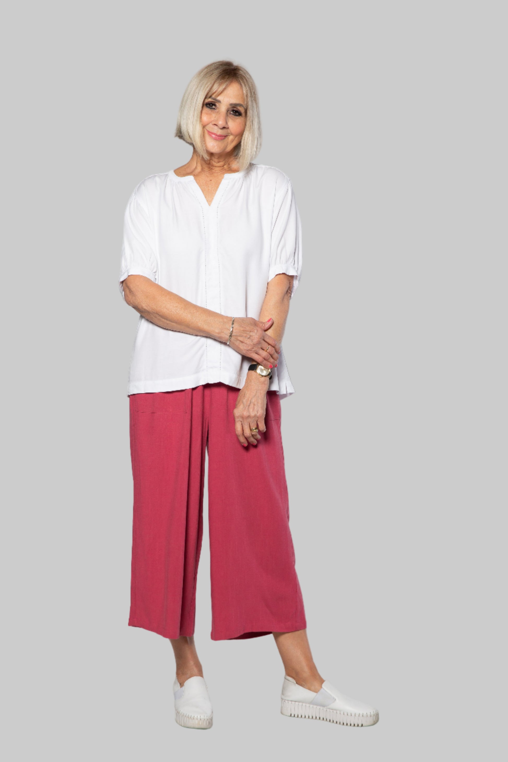 Woman wearing a white blouse and pink pants against a white background