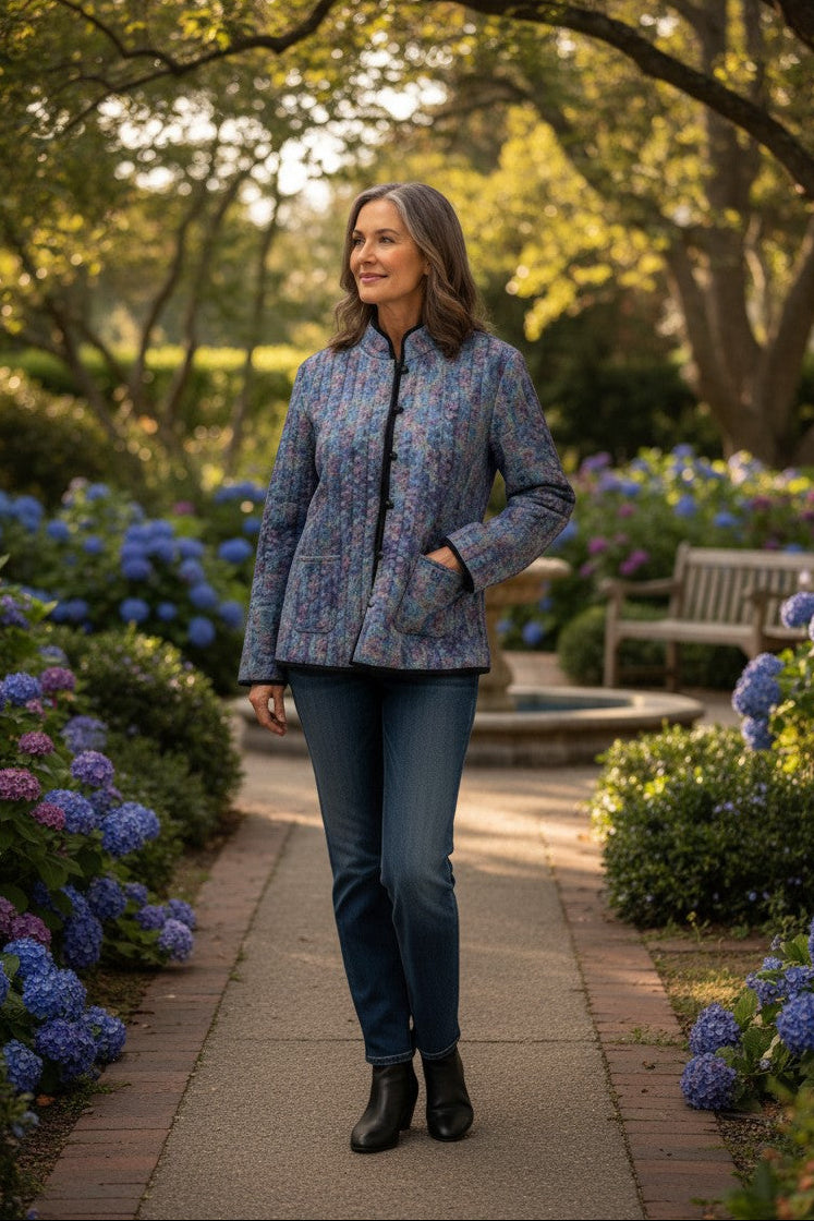 Model wearing Equinox Clothing reversible oriental jacket in blue floral print with patch pockets in a garden setting.