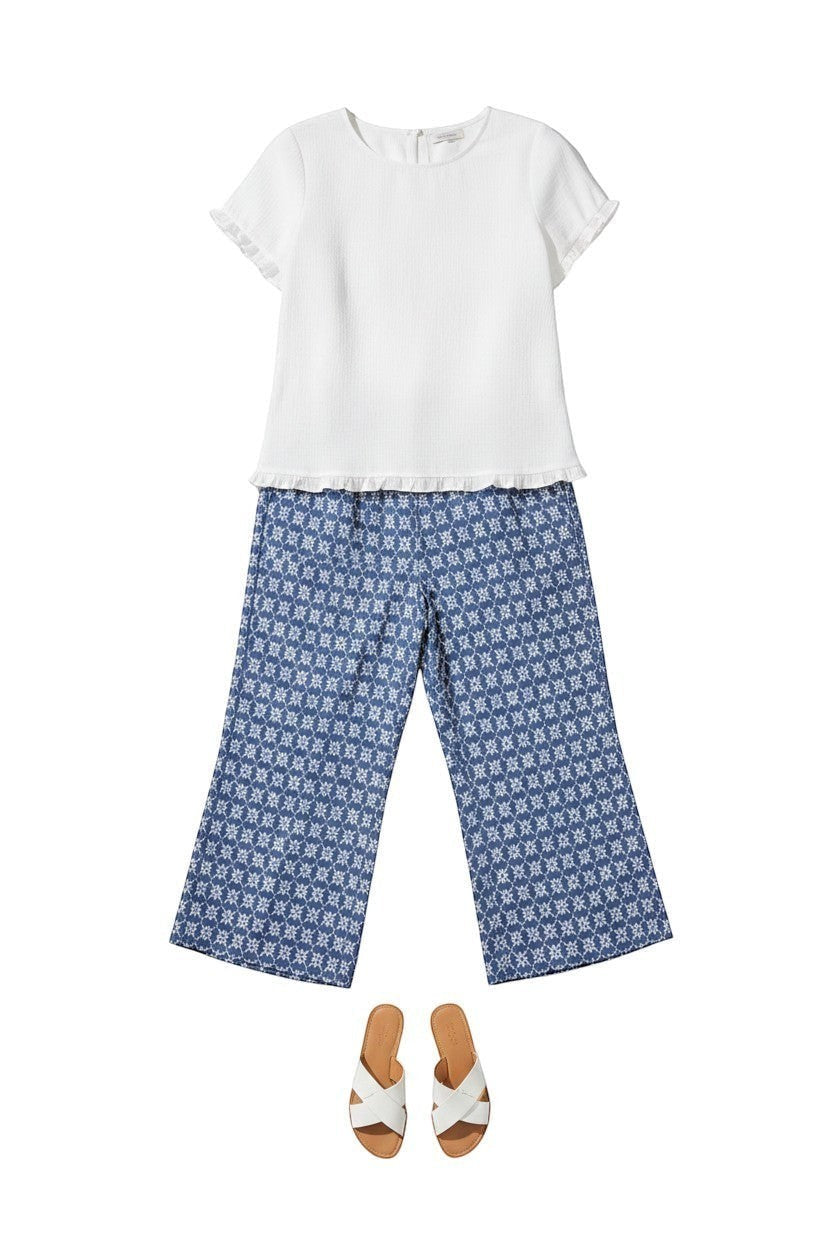 Equinox Clothing white Tencel ruffle trim top paired with blue patterned cropped pants and white slide sandals.