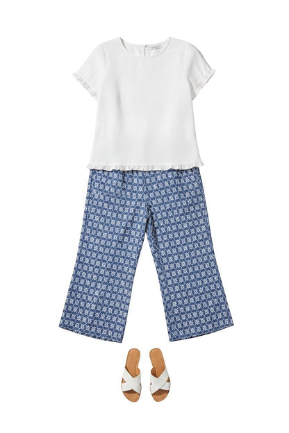Equinox Clothing white Tencel ruffle trim top paired with blue patterned cropped pants and white slide sandals.