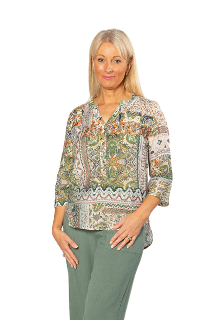 Woman wearing a patterned blouse and green pants on a white background