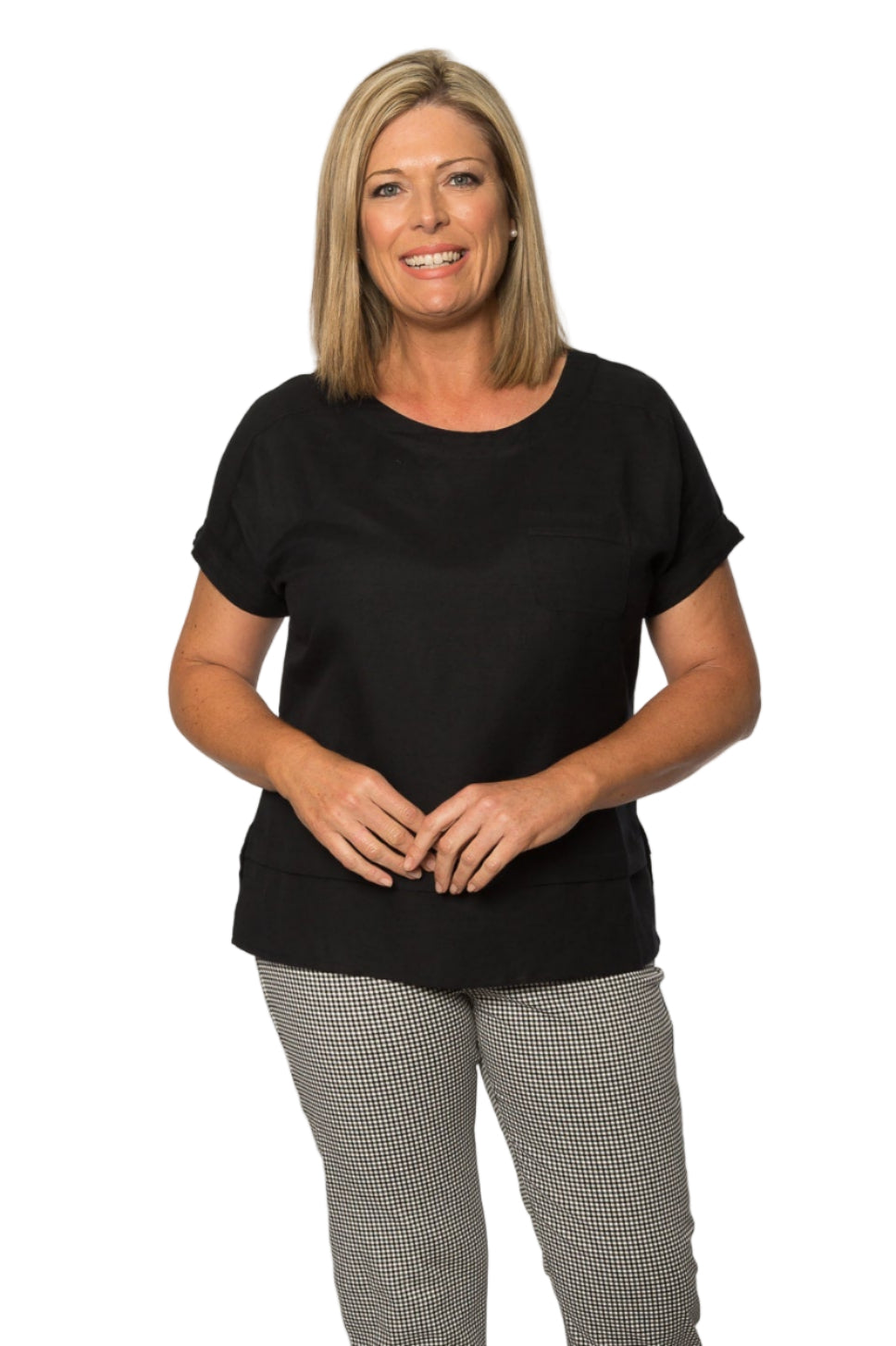 A woman standing against a white background wearing a black short sleeve viscose top with a double hemline and cuffs, paired with grey trousers.