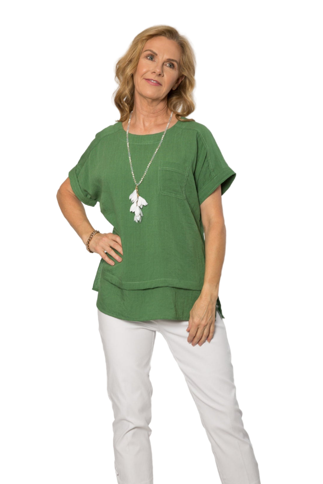 A woman wearing a green short sleeve viscose top with a double hemline, paired with white trousers. Accessories include a necklace and earrings.