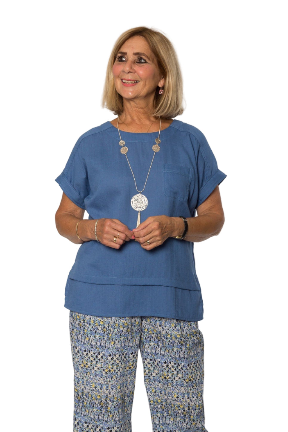 A woman wearing a blue short sleeve viscose top with a double hemline, paired with patterned wide-leg pants.