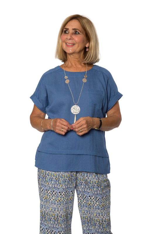 A woman wearing a blue short sleeve viscose top with a double hemline, paired with patterned wide-leg pants.